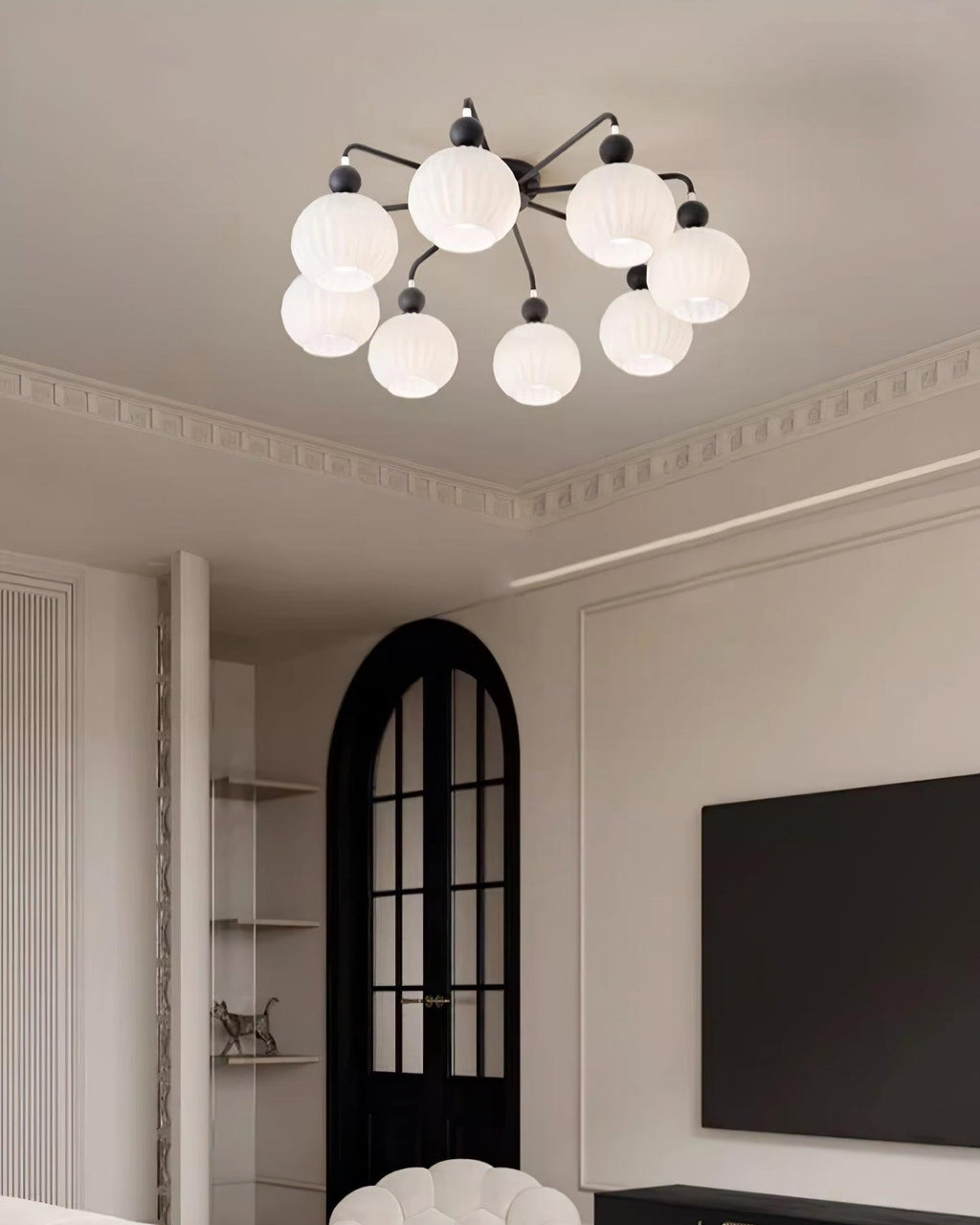 Eight-globe Clérachic ceiling light with black arms in a lounge with cornice mouldings, an arched black door and a wall-mounted TV.