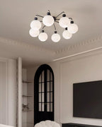Eight-globe Clérachic ceiling light with black arms in a lounge with cornice mouldings, an arched black door and a wall-mounted TV.