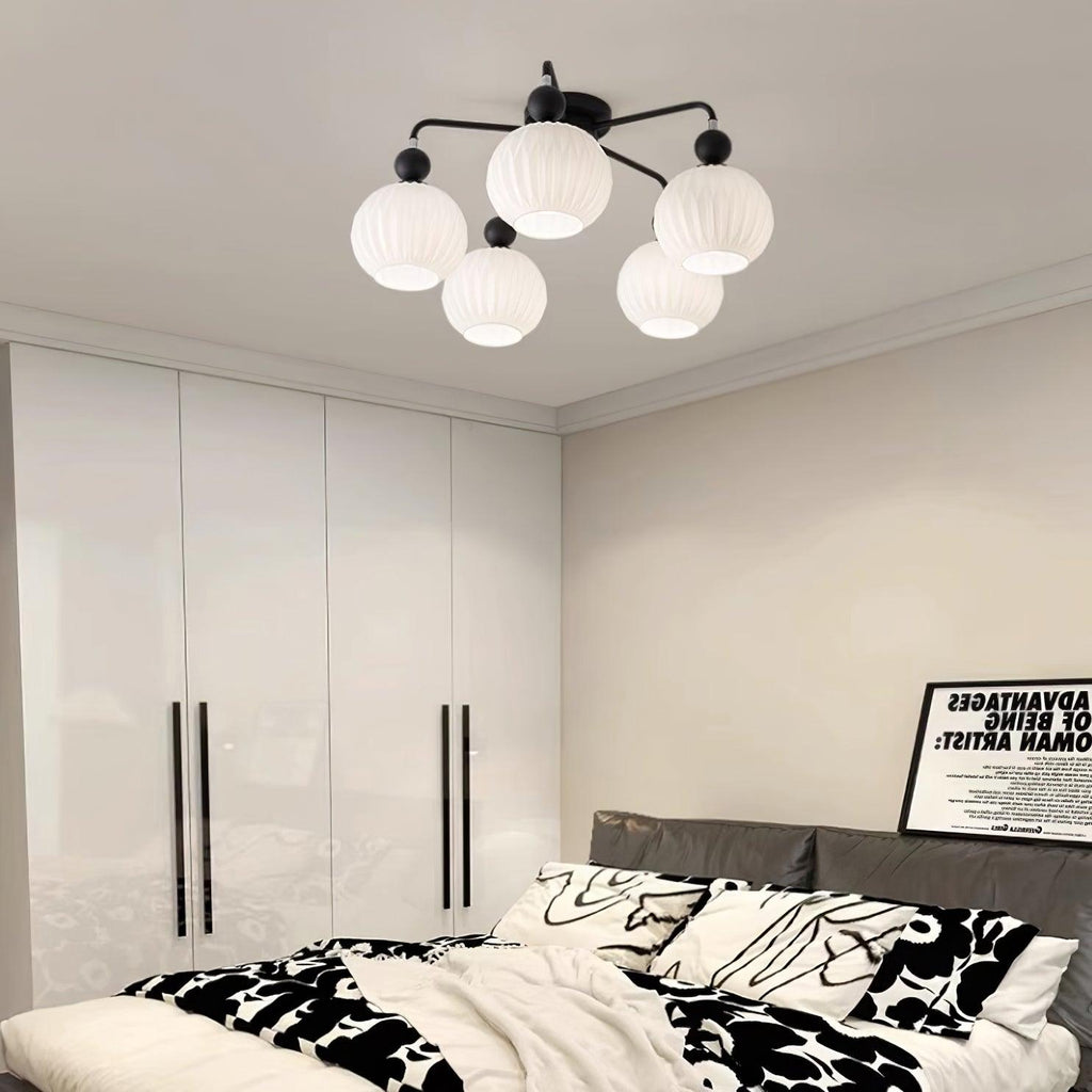 Black five-globe Clérachic ceiling light above a bedroom with a tall white wardrobe and black-and-white patterned bedding.