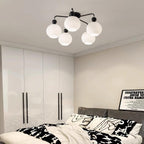 Black five-globe Clérachic ceiling light above a bedroom with a tall white wardrobe and black-and-white patterned bedding.