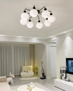 A Clérachic eight-globe ceiling light with black arms, in a bright room with a cream lounge chair and a TV unit.