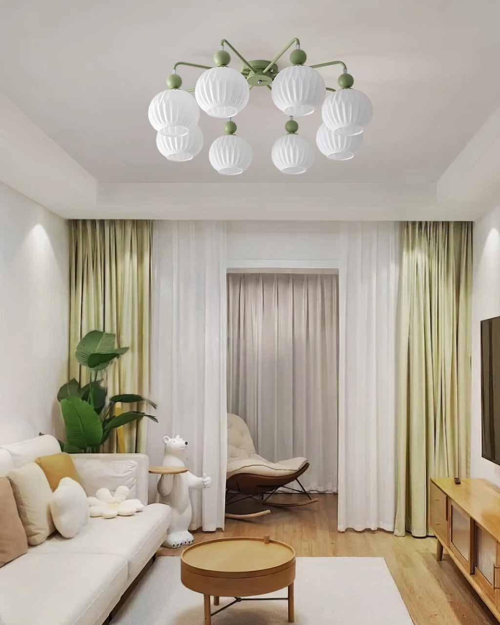 Green-armed Clérachic ceiling light over a living room with sage curtains, a round wood table and a pale sofa.