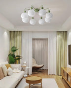 Green-armed Clérachic ceiling light over a living room with sage curtains, a round wood table and a pale sofa.