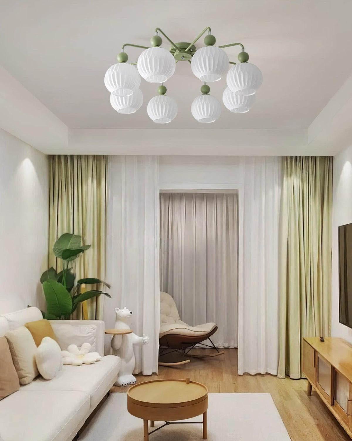 Green-armed Clérachic ceiling light over a living room with sage curtains, a round wood table and a pale sofa.