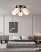Black five-globe Clérachic ceiling light above a grey upholstered bed, with a line-art panel on the wall behind it.
