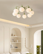 A green Clérachic ceiling light with eight ribbed globes, in a cream room with arched shelving and a beaded pendant.