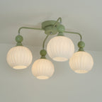 Lit four-globe Clérachic ceiling light in green, the ribbed globes glowing a warm white on arms with small green balls.