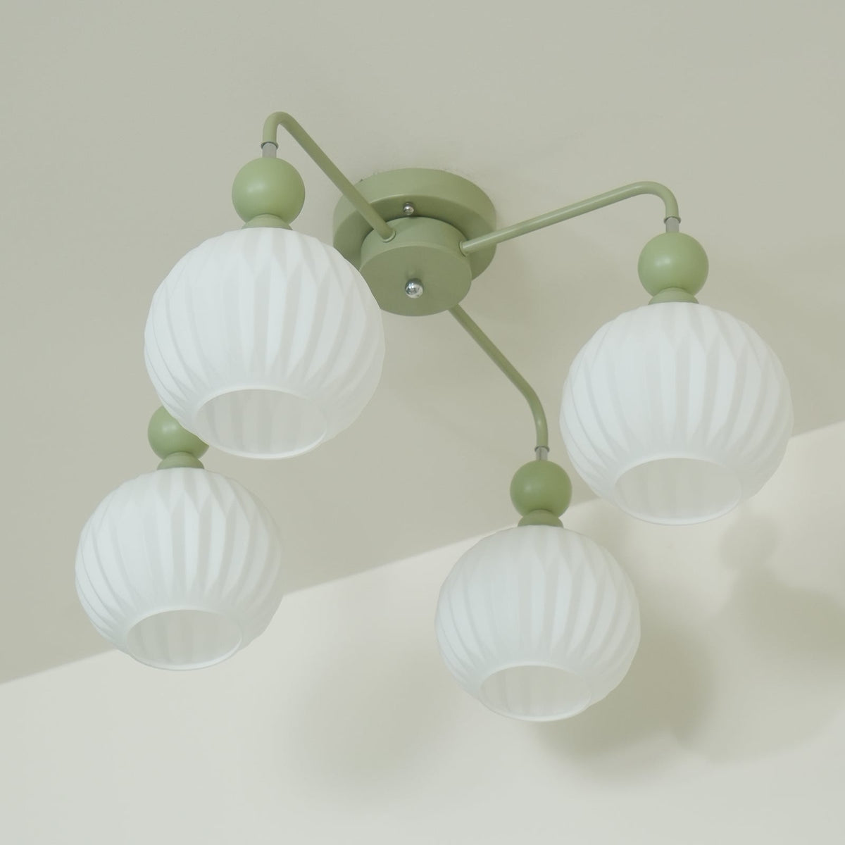 Underside view of the four-globe green Clérachic ceiling light, the ribbed white globes unlit against a pale wall.