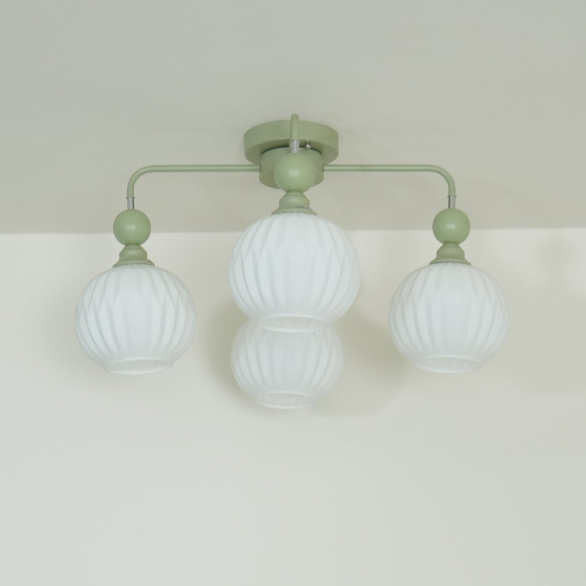 Low angle on a green Clérachic ceiling light with four unlit ribbed globes, two of them overlapping at the centre.