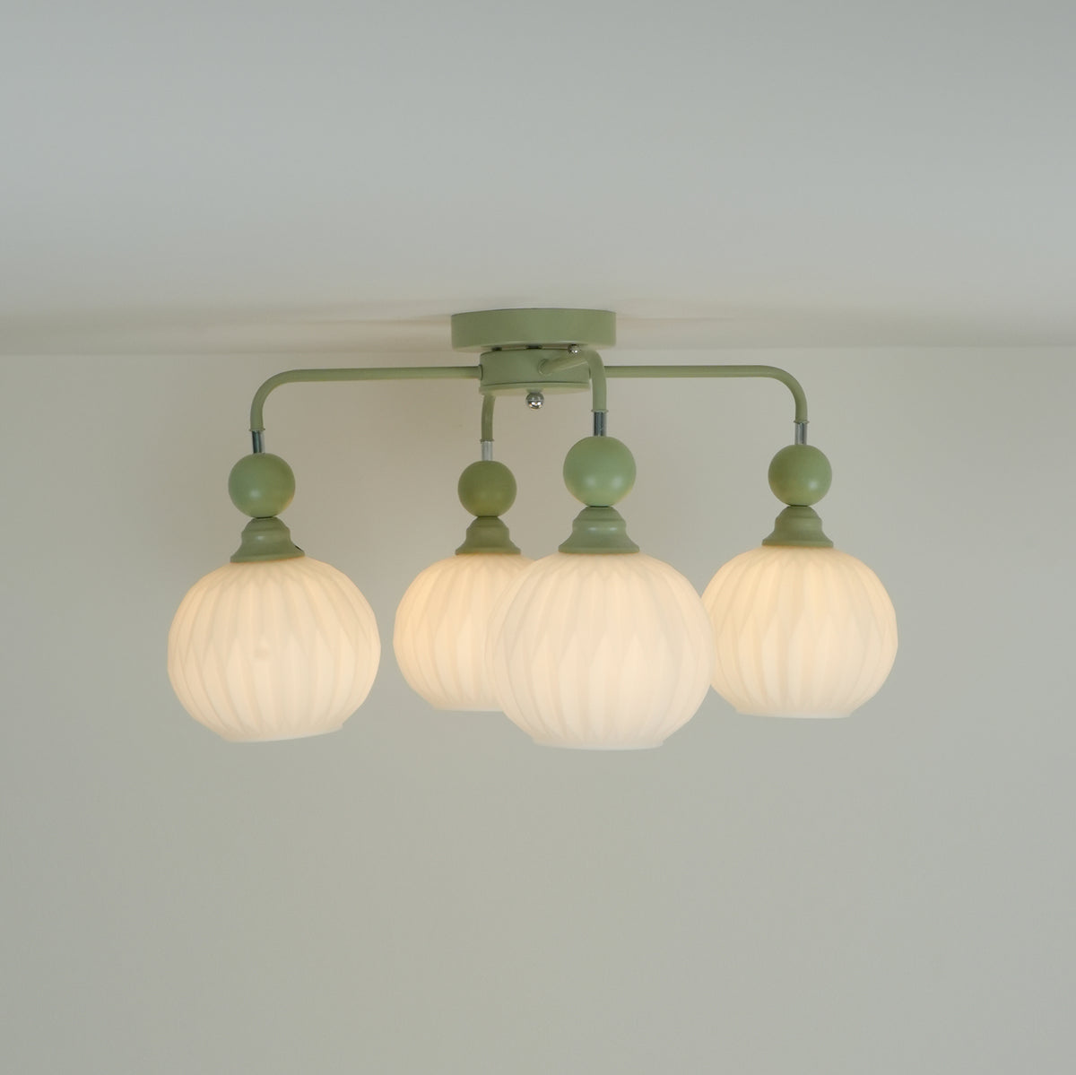 The four-globe Clérachic ceiling light switched on, its ribbed globes giving off a soft, warm glow below green arms.