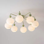 Lit eight-globe Clérachic ceiling light in green, the ribbed globes glowing warm on a pale ceiling.