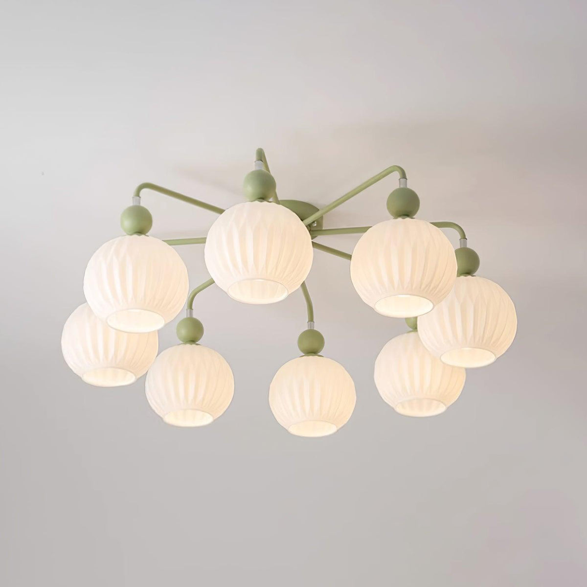 Lit eight-globe Clérachic ceiling light in green, the ribbed globes glowing warm on a pale ceiling.