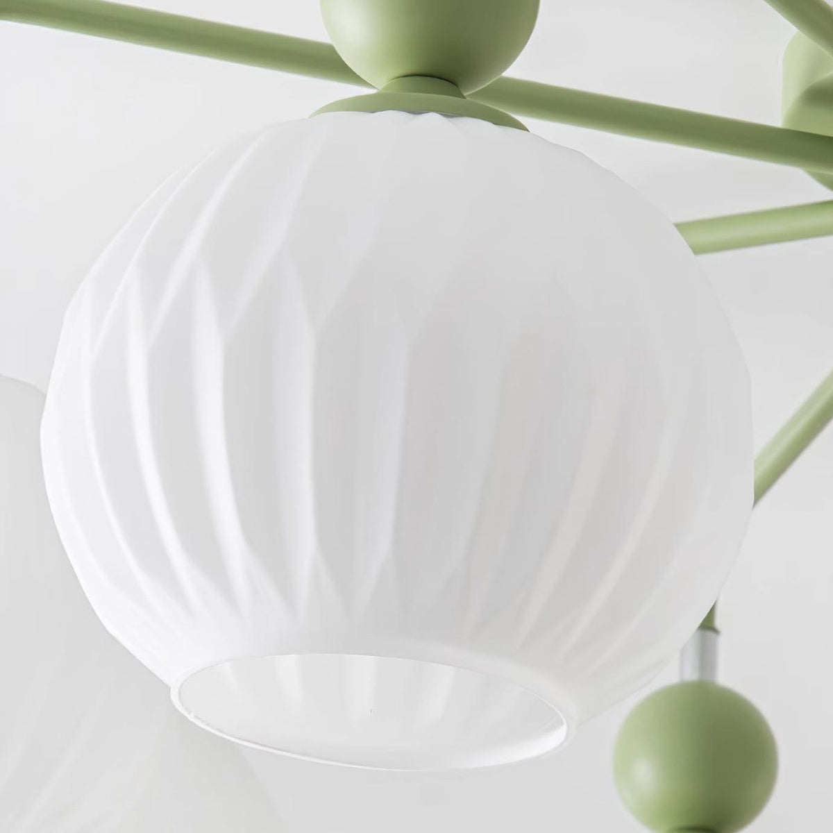 Close view of a ribbed frosted glass globe, its open rim and a green ball on the arm of this Clérachic ceiling light.