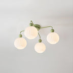 Lit four-globe Clérachic ceiling light in green, with warm light inside each ribbed globe on a pale grey ceiling.
