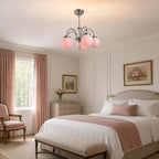 Pink globe glass Clérachic chandelier hanging in a pale bedroom with rose curtains and a white bed with a blush throw.