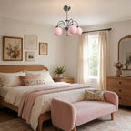 Pink-globed Clérachic chandelier over a wooden bed with a pink throw and a rose-pink bench, beside a sunlit window.