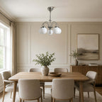 This Clérachic chandelier with white globes hangs over a long oak dining table with grey chairs, in a panelled room with a landscape print.