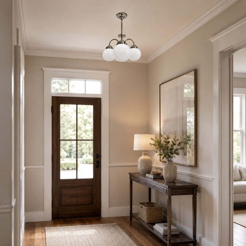 White globe Clérachic chandelier in a hallway, with a glazed wooden front door, a console table, a table lamp and a tall mirror.
