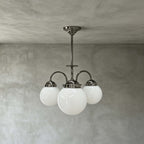 Three opal white glass globes on curved polished metal arms, this Clérachic chandelier hangs from a short rod against grey limewash.