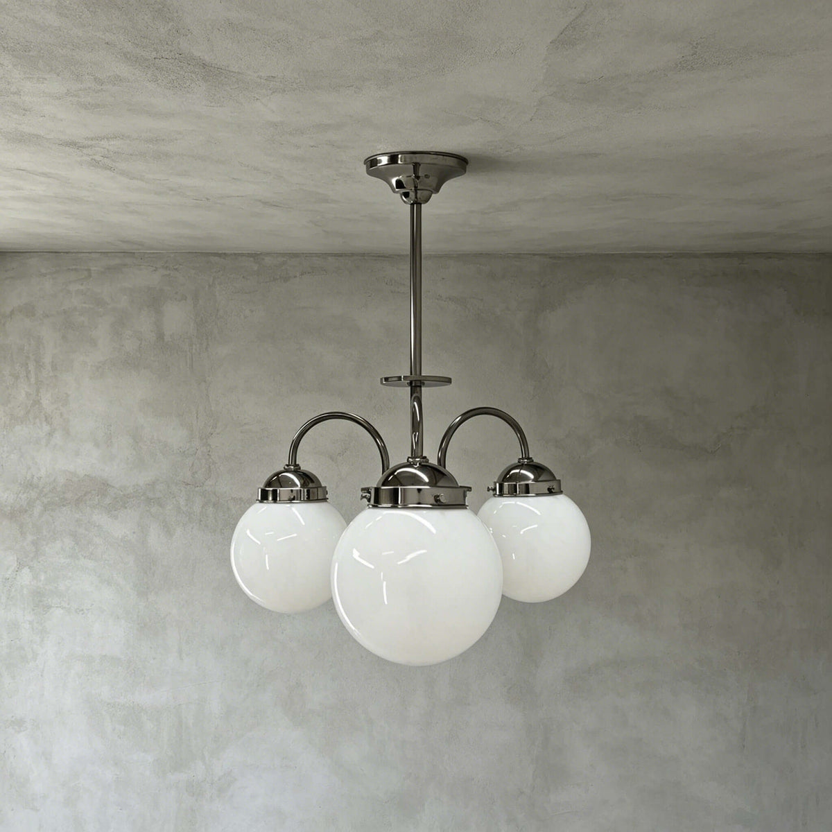 Three opal white glass globes on curved polished metal arms, this Clérachic chandelier hangs from a short rod against grey limewash.
