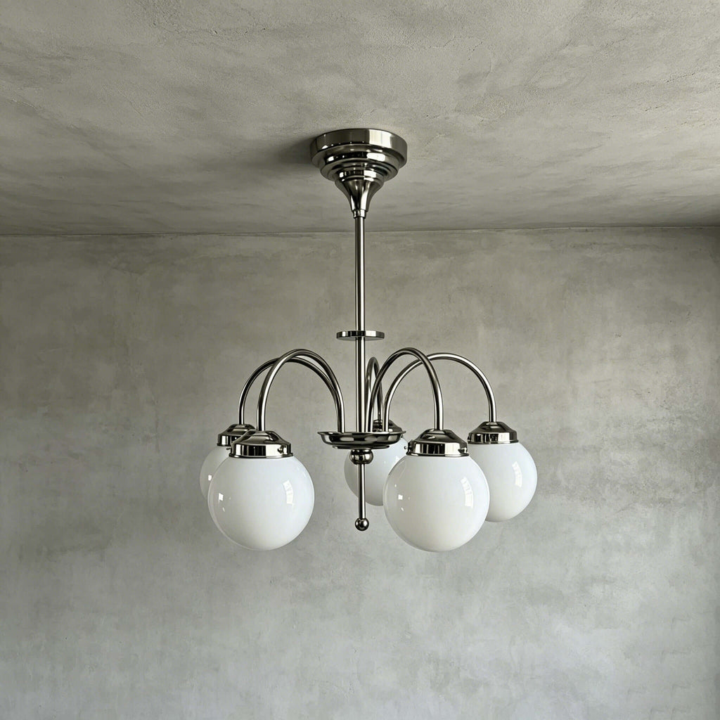Five white glass globes on curved polished metal arms form this Clérachic chandelier, shown hanging from a rod against a grey limewash wall.