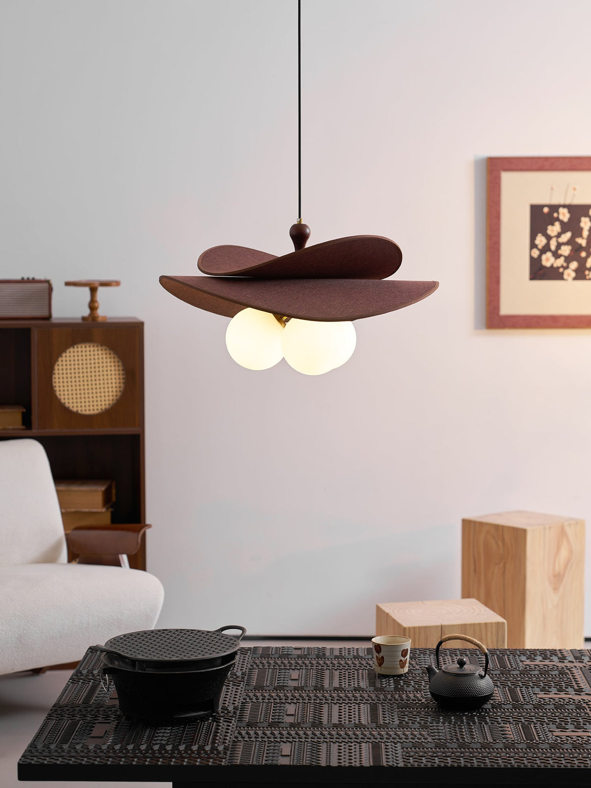 This Clérachic pendant hangs above a dark woven table with a cast-iron pot and teapot, beside a pale sofa and a cane-fronted cabinet.