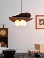 Closer view of a Clérachic pendant with brown fabric petals and two visible opal globes, hung over a dark table with a black iron kettle.