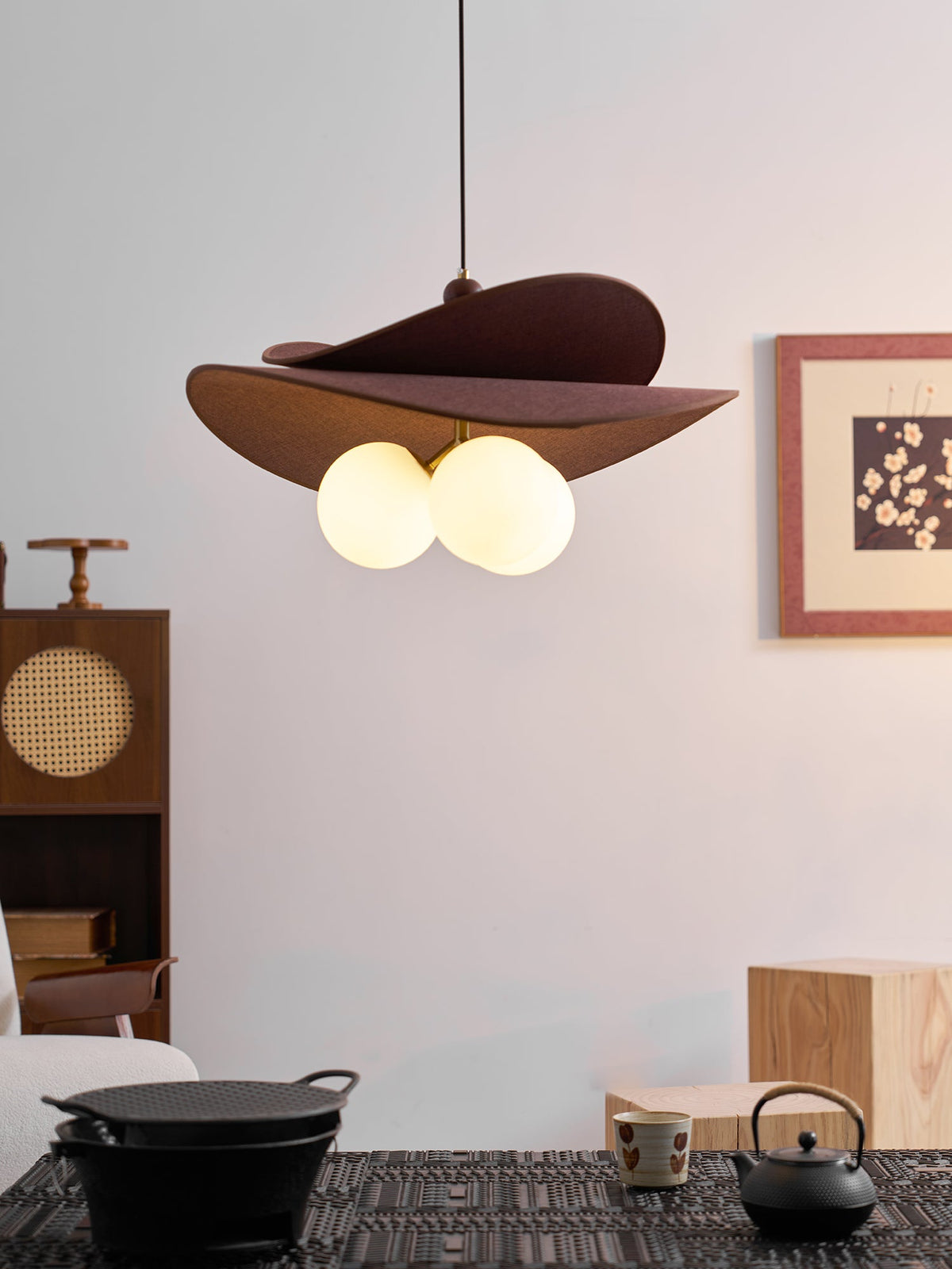 Closer view of a Clérachic pendant with brown fabric petals and two visible opal globes, hung over a dark table with a black iron kettle.