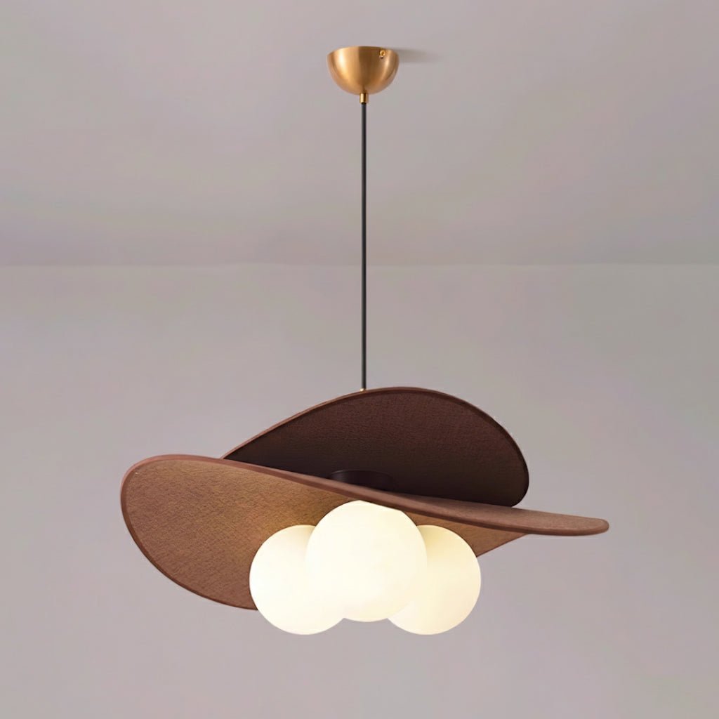 Brown fabric petals tilted over three white globes on a Clérachic pendant, hung from a brass canopy against a pale lilac wall.