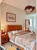 This Clérachic pendant glows above a bedroom with a tan tufted headboard, floral bedding and a clothes rail in the corner.