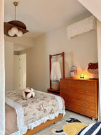 Clérachic pendant on a brass canopy in a corner of a bedroom, with a warm orange chest of drawers and a floral bedspread below.