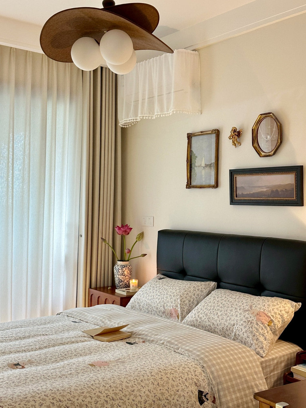 Brown-petalled Clérachic pendant seen close to the ceiling above a bed with a black headboard and a cream curtain at the left.
