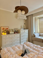 This Clérachic pendant hangs in a cream bedroom above white chests of drawers, a bay window seat and a quilt with a laptop on it.