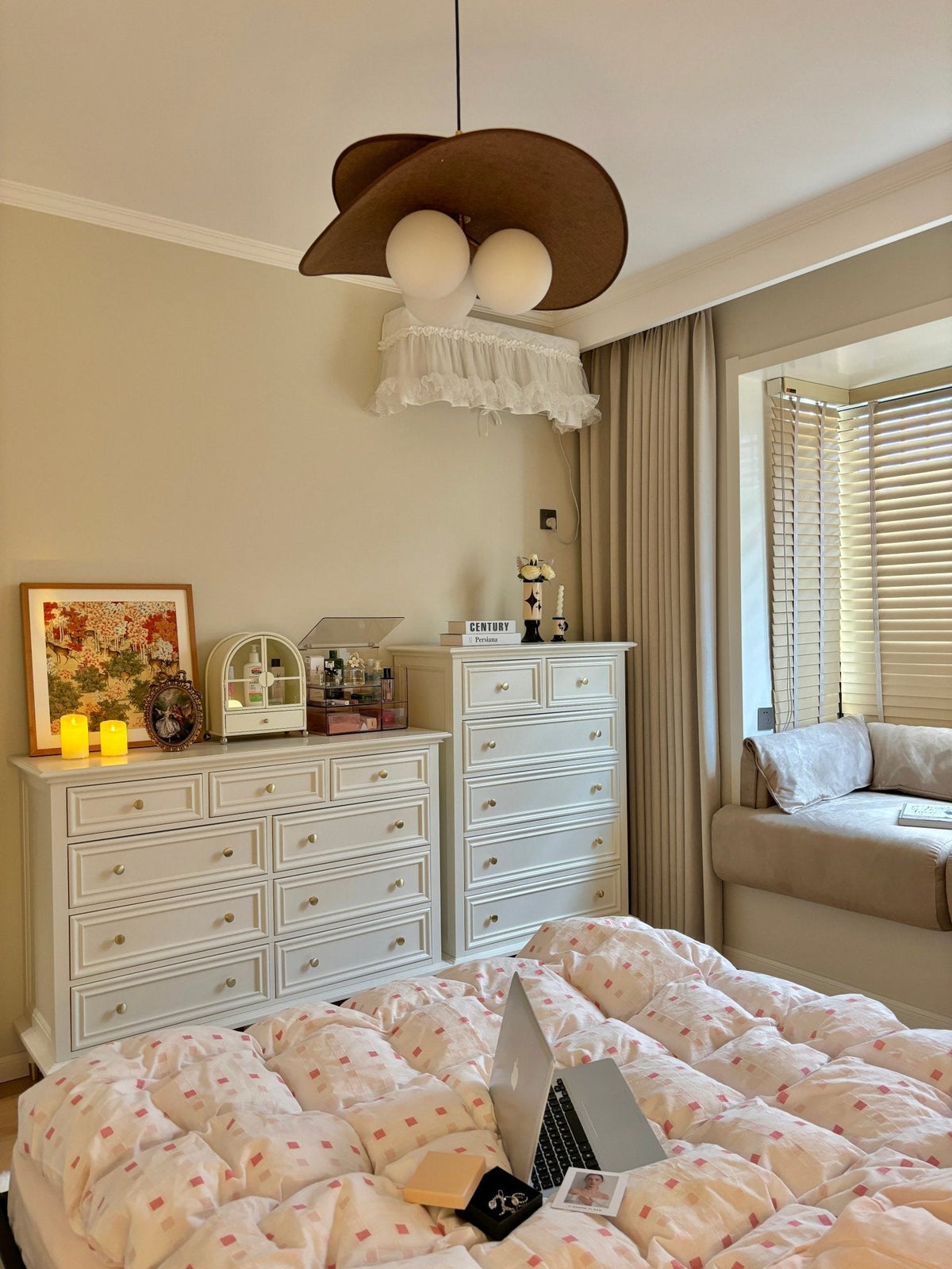 This Clérachic pendant hangs in a cream bedroom above white chests of drawers, a bay window seat and a quilt with a laptop on it.