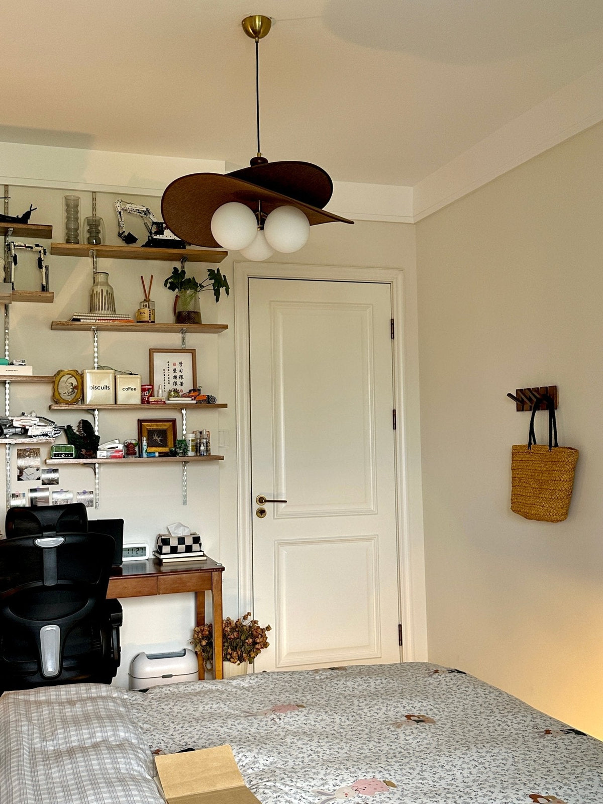 Clérachic pendant hung in a study-bedroom with open shelves, a white door and a woven bag on the wall.