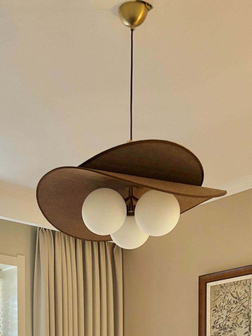 Looking up at a Clérachic pendant with a brass canopy, brown petals and three white globes, with beige curtains behind it.
