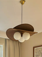 Looking up at a Clérachic pendant with a brass canopy, brown petals and three white globes, with beige curtains behind it.