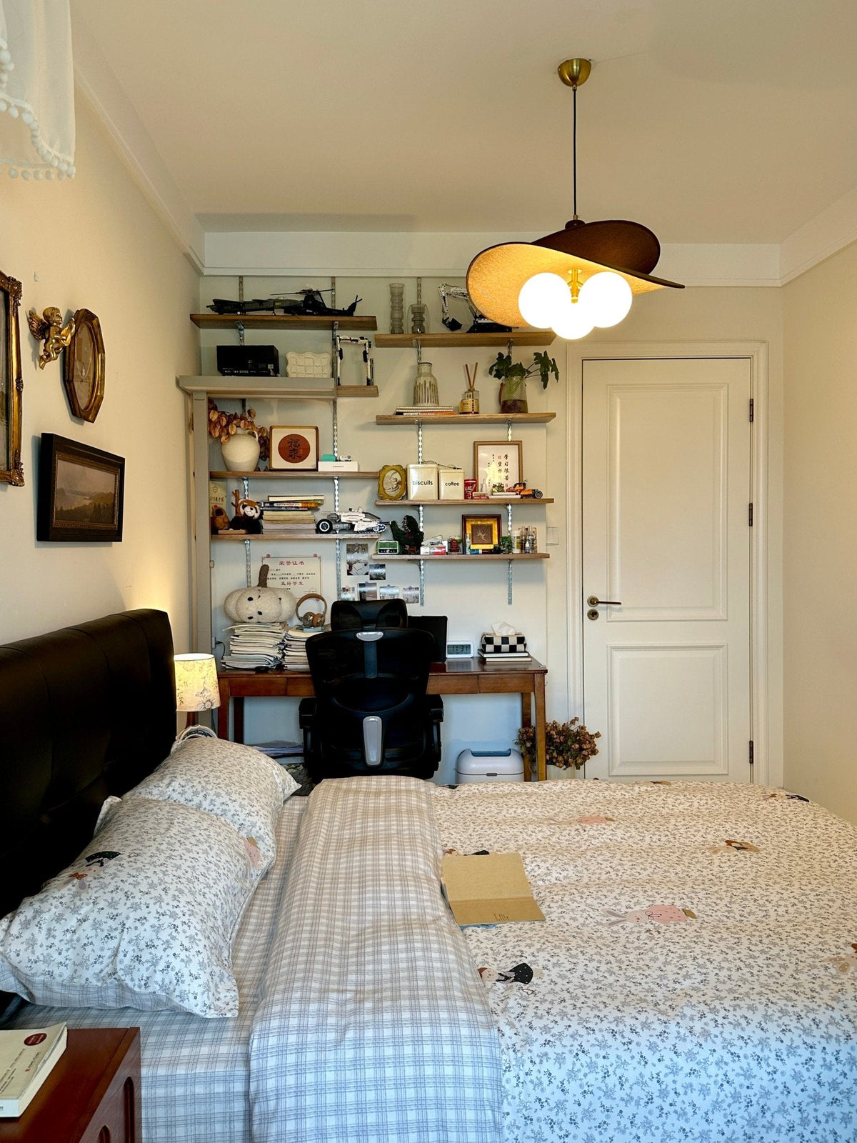 Clérachic pendant glowing warm above a bed with checked bedding, a black headboard and a shelving unit beside a white door.