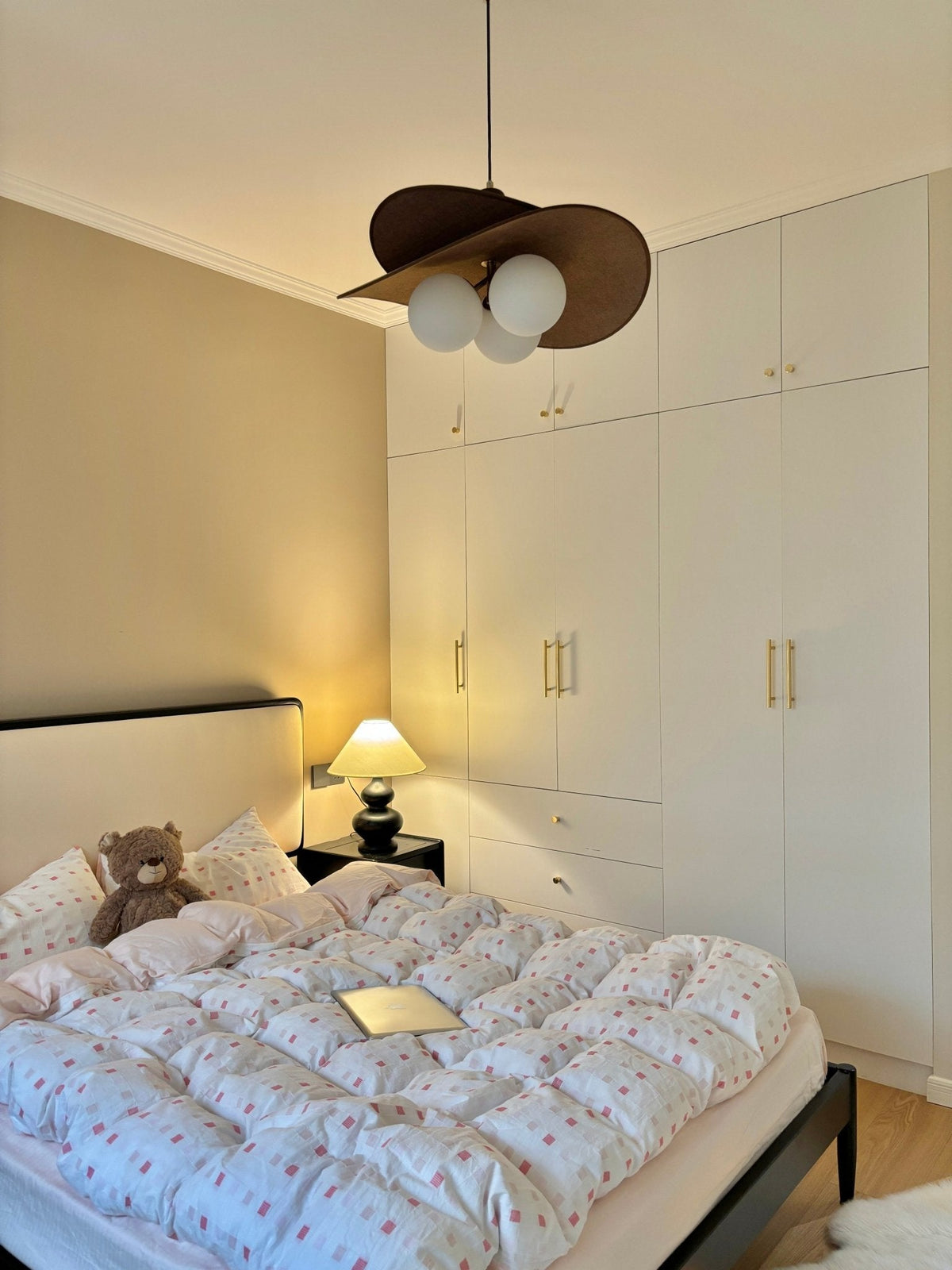 This Clérachic pendant hangs near a wall of white wardrobes above a bed with a bear and a bedside lamp glowing.