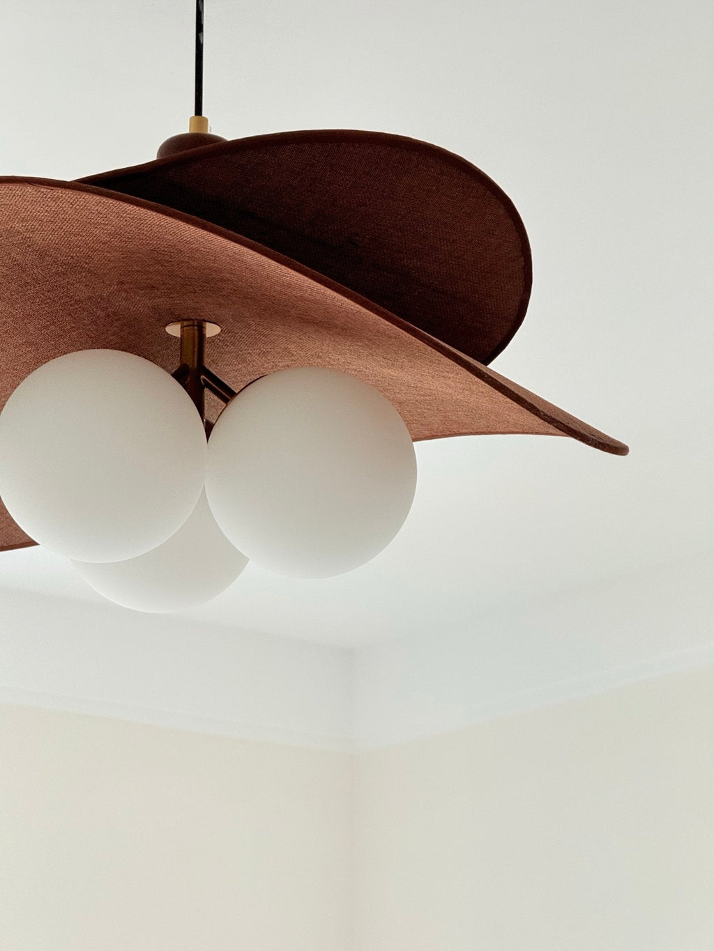 Close view of this Clérachic pendant's brown felt-like petal and three opal globes against a plain white ceiling corner.