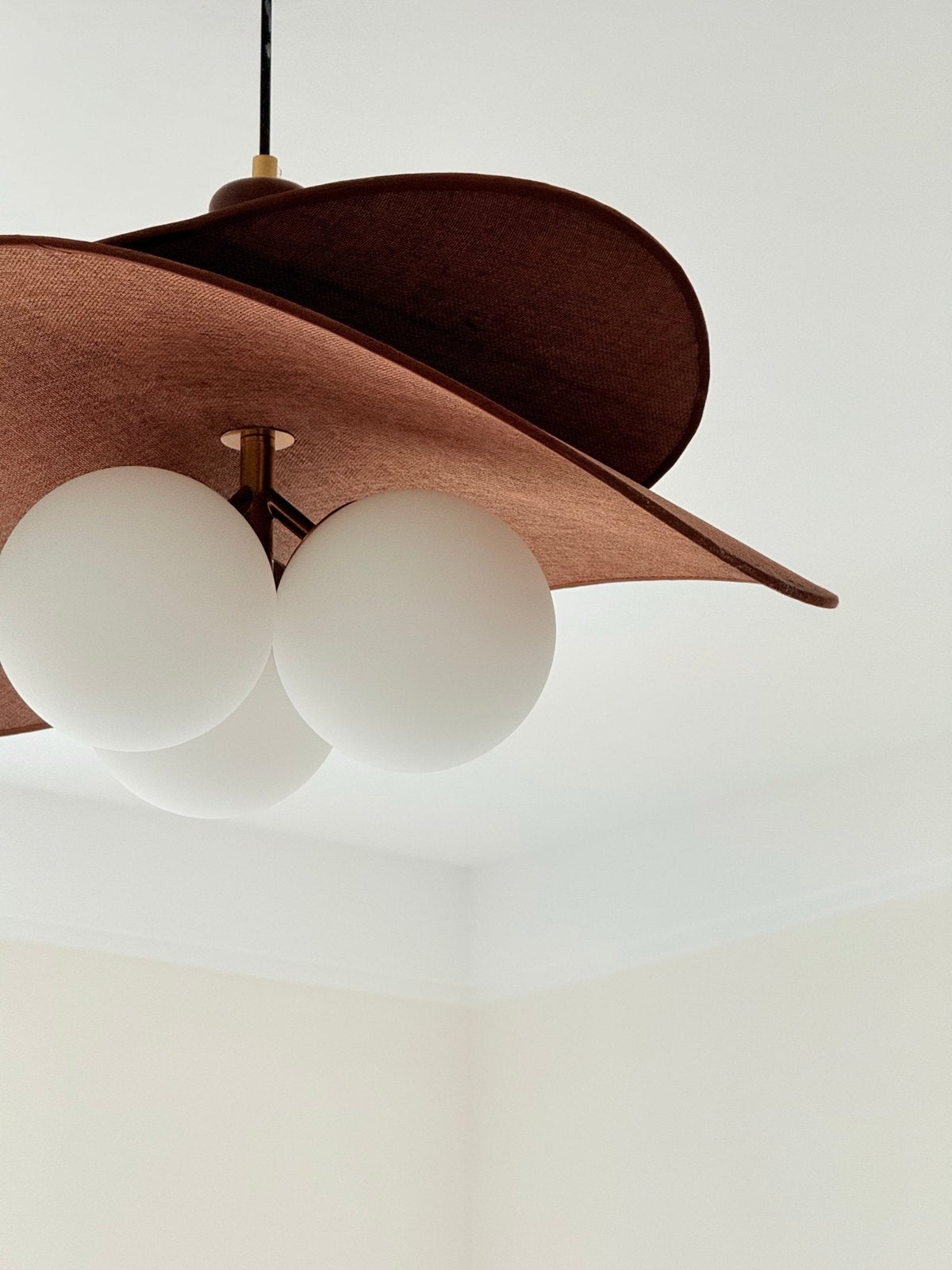 Close view of this Clérachic pendant's brown felt-like petal and three opal globes against a plain white ceiling corner.