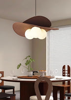 Clérachic pendant with a warm glow above a round dining table with dark wood chairs, a plant and a window with white blinds.