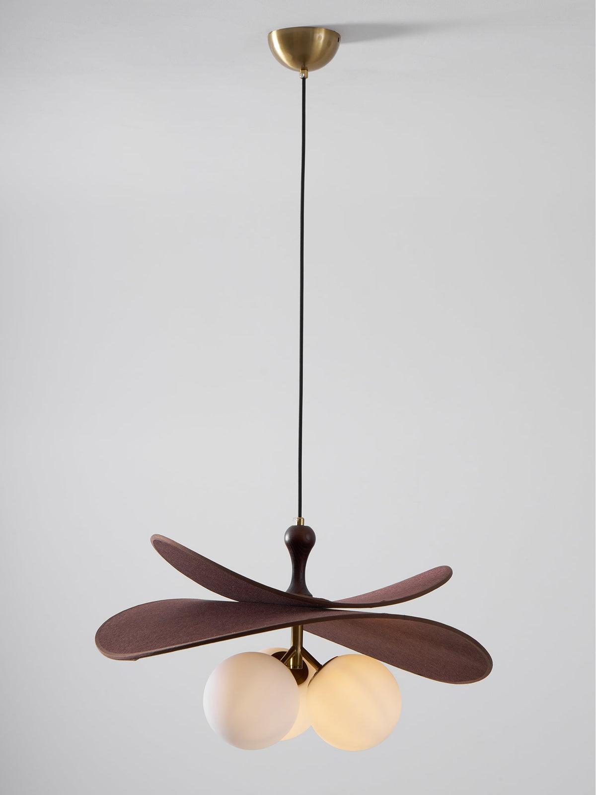 This Clérachic pendant hangs on a long black cord from a brass canopy against a pale grey backdrop, with its globes softly lit.