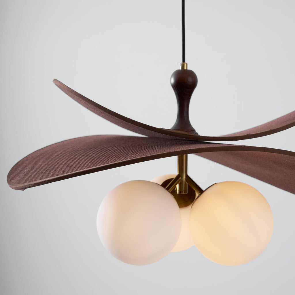 Straight-on view of a Clérachic pendant with warm light in its globes, brown fabric petals and a polished brass stem.