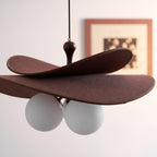 Close view of the brown fabric petals and two white opal globes on a Clérachic pendant, with a framed print blurred behind.