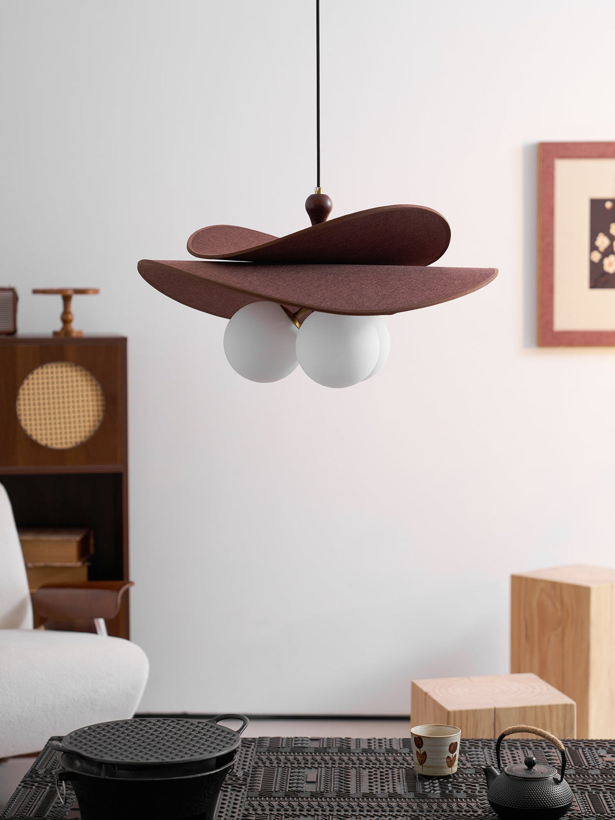 Unlit Clérachic pendant hung above a dark woven table with an iron pot, a cane-fronted cabinet and a pale sofa.