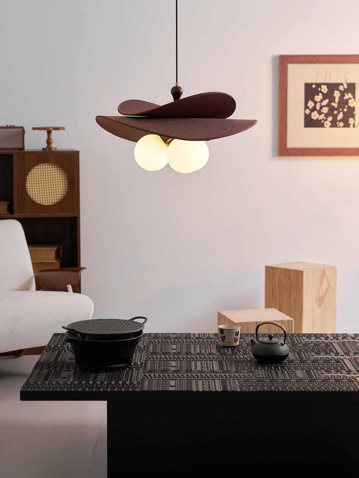 Clérachic pendant lit above a dark low table with a black iron pot and teapot, with a wooden cabinet and framed print behind.
