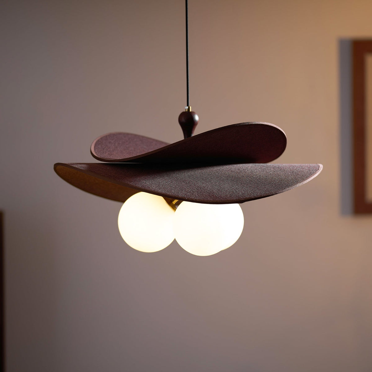 Close view of a Clérachic pendant lit in a dim room, with warm light from three globes under the layered brown petals.