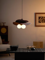 Clérachic pendant glowing in evening light above a dark low table with a teapot, with a framed print on the wall behind.