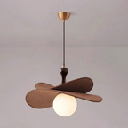 This Clérachic pendant on a brass canopy with a single lit globe visible under two brown petals, against a soft pink-grey wall.